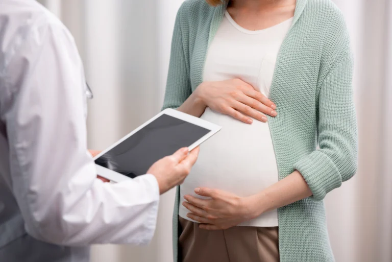 partial view of doctor and pregnant woman discussing pregnancy process together in clinic